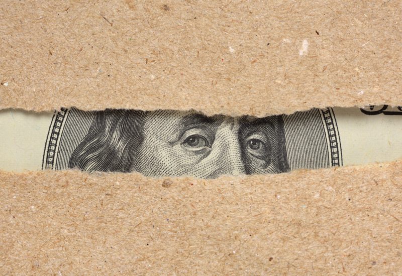 One hundred dollar bill behind brown craft ripped paper One hundred dollar bill Benjamin Franklin portrait looks behind brown craft ripped paper